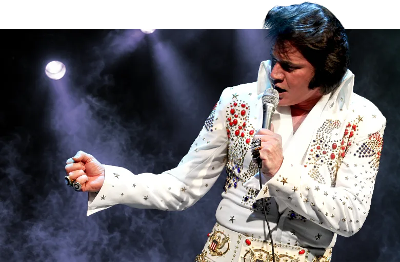 Edson Galhardi no palco, de macacão branco bordado, cantando ao microfone