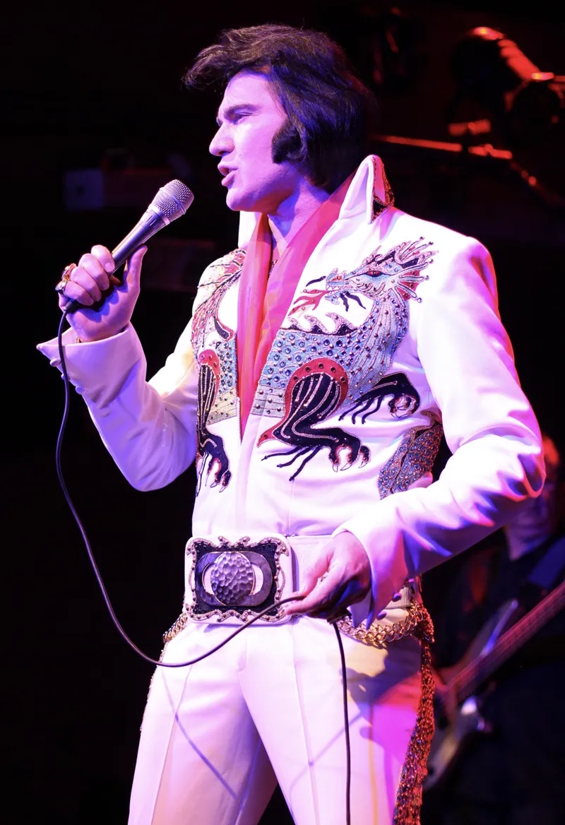 Edson Galhardi cantando no palco com macacão branco bordado
